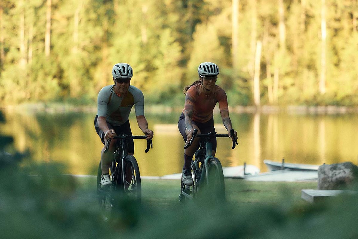 Två cyklister. I bakgrunden en skog som speglar sig i en sjö.